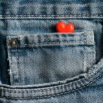 Close-up image of a red heart nestled in a blue denim jean pocket, symbolizing love and fashion.