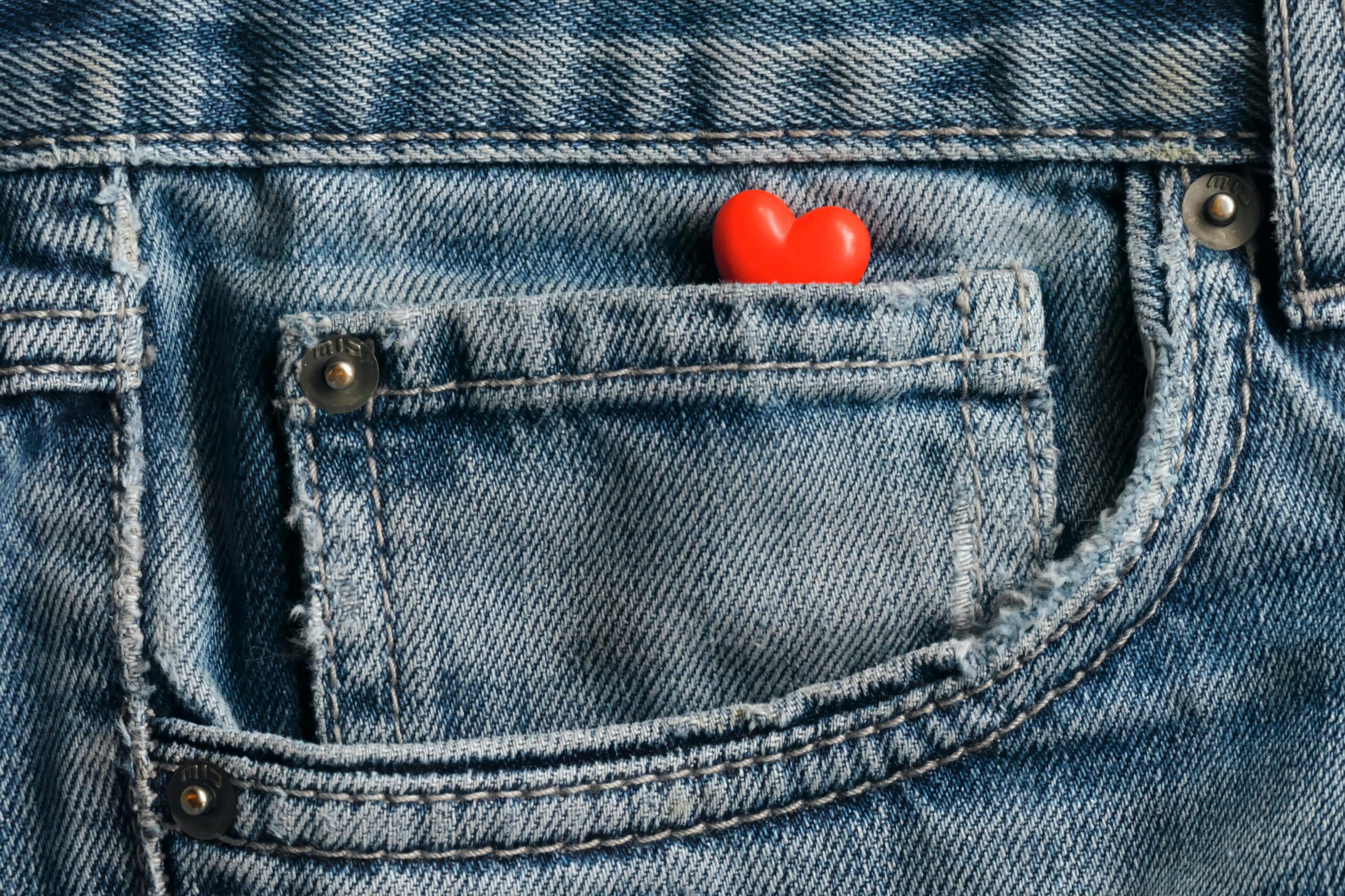 Close-up image of a red heart nestled in a blue denim jean pocket, symbolizing love and fashion.