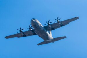 A C-130 Hercules military aircraft soaring in clear blue skies.