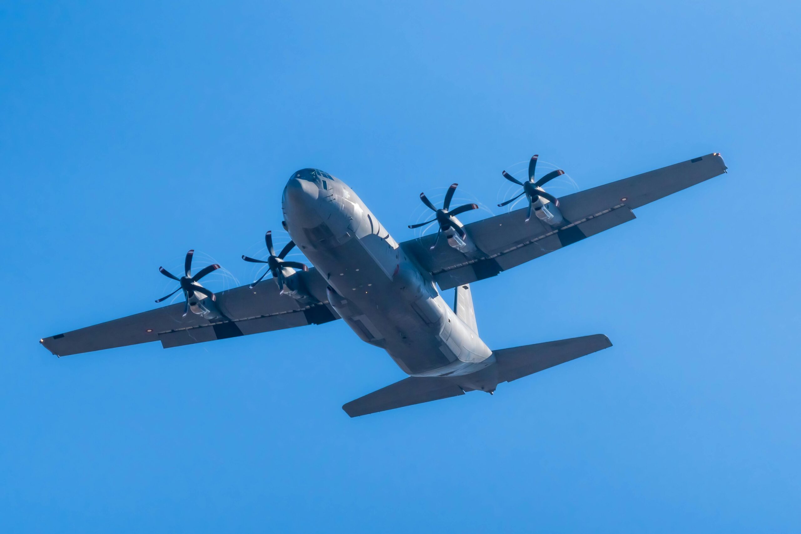 A C-130 Hercules military aircraft soaring in clear blue skies.